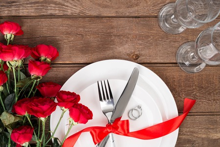 Top view closeup of romantic dinner serving with a bouquet  red roses and ring above the white plateの写真素材