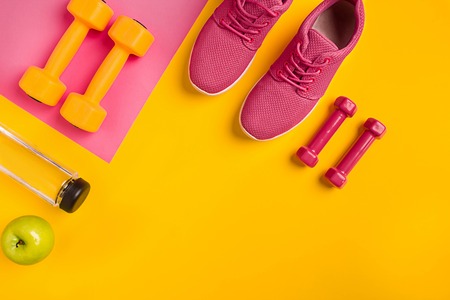 Athletes set with female clothing, dumbbells and bottle of water on yellow backgroundの写真素材