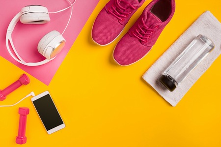 Fitness accessories on a yellow background. Sneakers, bottle of water, earphones and dumbbells.の写真素材