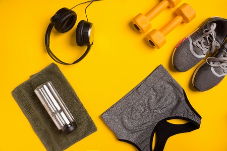 Fitness accessories on a yellow background. Sneakers, bottle of water, smart, towel and sport top.の写真素材