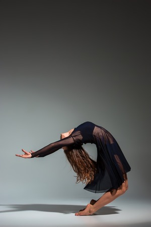 Young beautiful dancer in black dress posing on a dark gray studio backgroundの写真素材