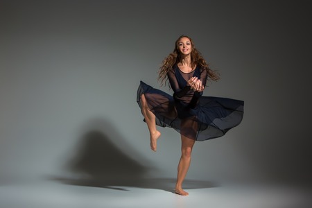 Young beautiful dancer in black dress posing on a dark gray studio backgroundの写真素材