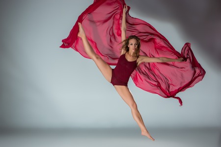 Young beautiful woman dancer in red swimsuit posing on a light grey studio backgroundの写真素材