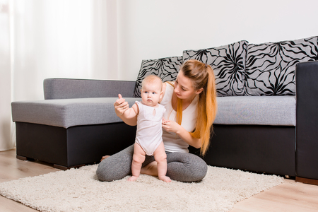 Happy young mother playing with her baby on the floor near the sofaの写真素材
