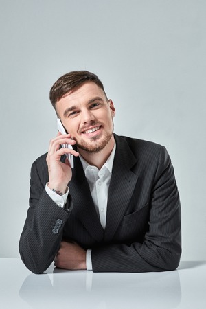 Handsome young man talking on the mobile phone while sitting at his working place in officeの写真素材
