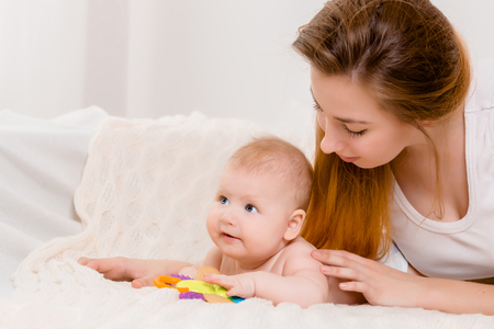 Mother and child on a white bed. Mom and baby boy in diaper playing in sunny bedroom.の写真素材