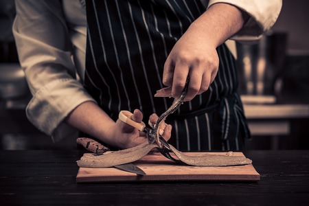 Chef cutting the fish on a board. Photo in brown tones. Kitchen. Wooden tableの写真素材
