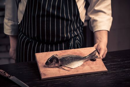 Chef cutting the fish on a board. Photo in brown tones. Kitchen. Wooden tableの写真素材