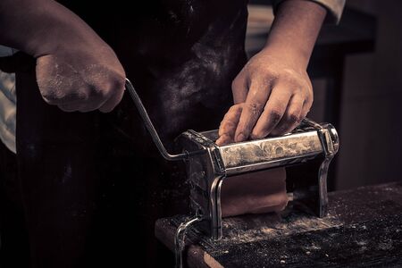 The chef makes fresh pasta from scratch. Wooden table. Photo in brown tones. Kitchen.の写真素材