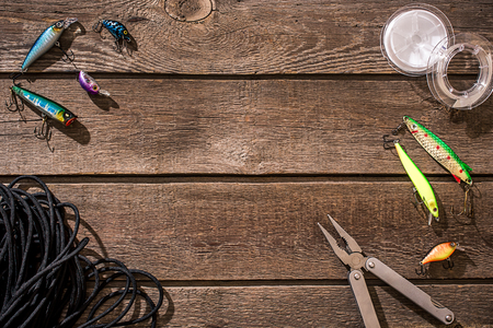 Accessories for fishing on the background of wood. Reel, fishing line, float, net hooks, lures for fishing. Top view. Still life. Copy spaceの写真素材