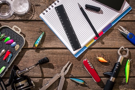 Accessories for fishing on the background of wood. Reel, fishing line, float, net hooks, lures for fishing. Top view. Still life. Copy spaceの写真素材