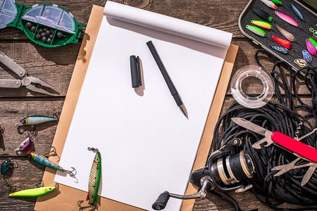 Accessories for fishing on the background of wood. Reel, fishing line, float, net hooks, lures for fishing. Top view. Still life. Copy spaceの写真素材