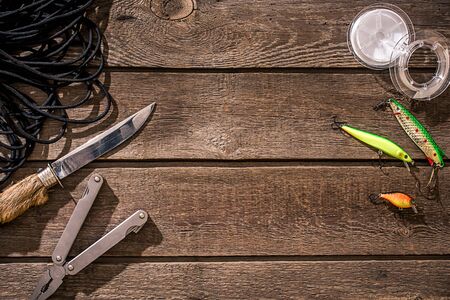 Accessories for fishing on the background of wood. Reel, fishing line, float, net hooks, lures for fishing. Top view. Still life. Copy spaceの写真素材