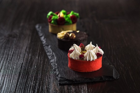 Side view on mini party tartlets with fresh fruit, chocolate, nuts and cream on black slate...