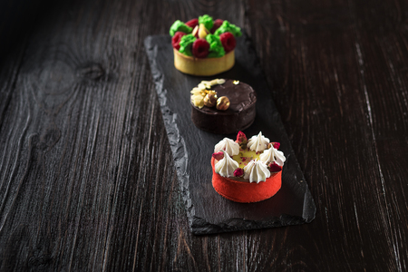 Side view on mini party tartlets with fresh fruit, chocolate, nuts and cream on black slate backgroundの写真素材