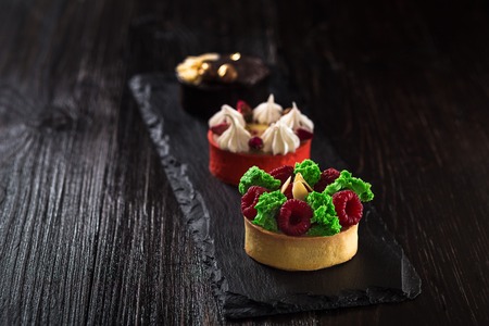 Side view on mini party tartlets with fresh fruit, chocolate, nuts and cream on black slate backgroundの写真素材