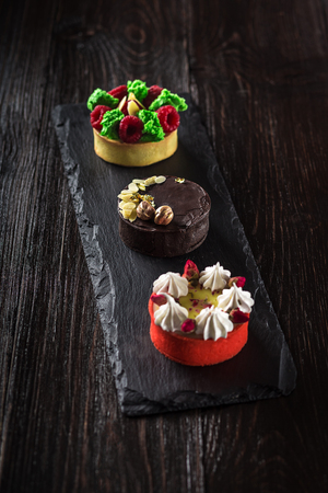 Side view on mini party tartlets with fresh fruit, chocolate, nuts and cream on black slate backgroundの写真素材