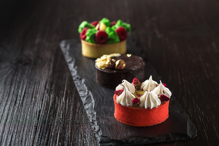 Side view on mini party tartlets with fresh fruit, chocolate, nuts and cream on black slate backgroundの写真素材