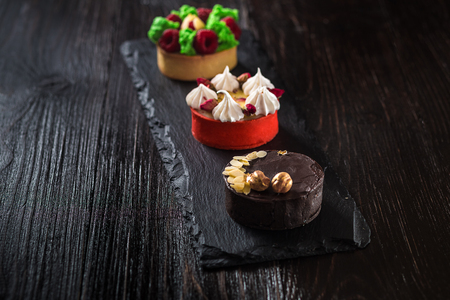 Side view on mini party tartlets with fresh fruit, chocolate, nuts and cream on black slate backgroundの写真素材