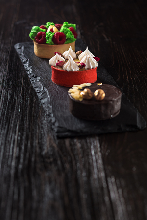 Side view on mini party tartlets with fresh fruit, chocolate, nuts and cream on black slate backgroundの写真素材