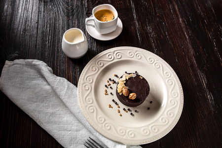 Beautiful decorated chocolate cake with golden nuts on a white plate and a cup of coffee on a black wooden backgroundの写真素材