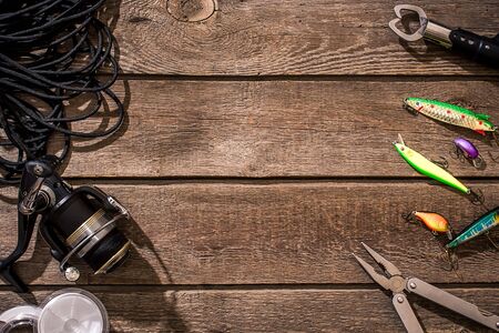 Fishing tackle - fishing spinning, fishing line, hooks and lures on wooden background. Top view. Copy space. Still lifeの写真素材