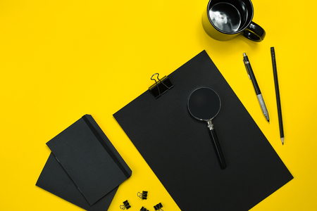 Flat lay display of business office gadgets with notepad, cup, pen, develop, glasses and etc. Top view display with copy space for display anything into images. Black office objects on a yellow backgroundの写真素材