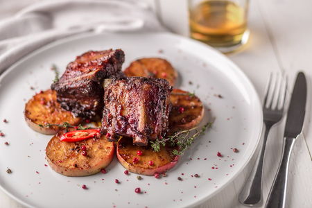 Hot Meat Dishes. Pork ribs grilled with peppers and apples on a white plate. Wooden background.の写真素材