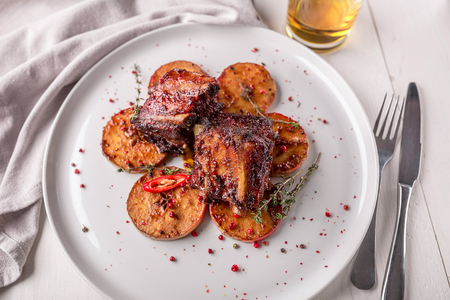 Hot Meat Dishes. Pork ribs grilled with peppers and apples on a white plate. Wooden background.の写真素材