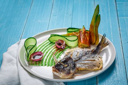 Fried fish dorado, decorated with cucumbers and onions. On a blue wooden backgroundの写真素材