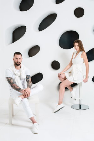 Casual couple near a white wall, man and woman in white clothing.の写真素材