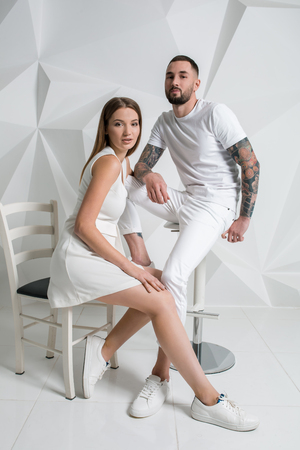 Casual couple near a white wall, man and woman in white clothing.の写真素材
