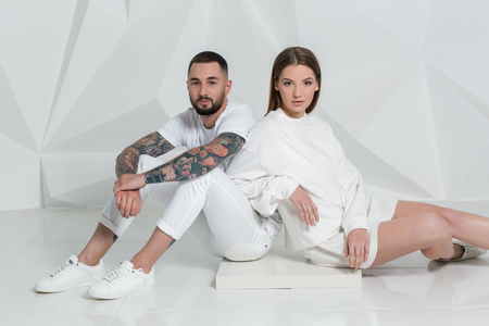 Casual couple near a white wall, man and woman in white clothing.の写真素材