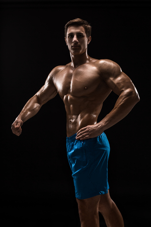Muscular and fit young bodybuilder fitness male model posing over black background.の写真素材