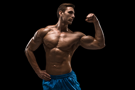 Muscular and fit young bodybuilder fitness male model posing over black background.の写真素材