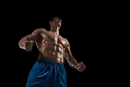 Muscular and fit young bodybuilder fitness male model posing over black background.の写真素材