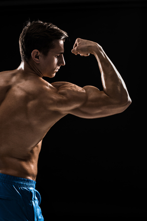Strong Athletic Man Fitness Model posing back muscles, triceps over black backgroundの写真素材