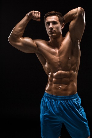Muscular and fit young bodybuilder fitness male model posing over black background.の写真素材