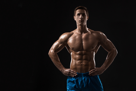 Muscular and fit young bodybuilder fitness male model posing over black background.の写真素材