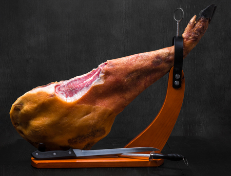 Whole jamon on a wooden stand on dark backgroundの写真素材