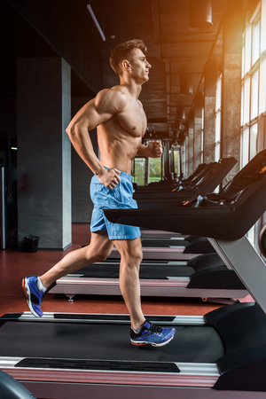 Young adult man running on treadmill in gymの写真素材