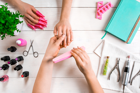 Manicure for the client. Close-up of the hands of a manicurist and client on a wooden backgroundの写真素材
