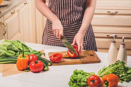 Young woman cooking in the kitchen at home. A woman cuts a pepper and vegetables with a knife.の写真素材