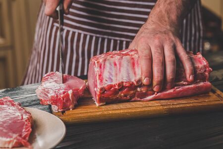 Man cuts of fresh piece of meat on a wooden cutting board in the home kitchenの写真素材