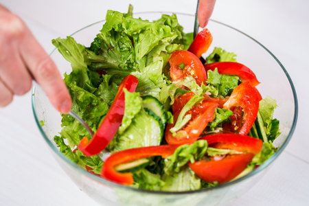 Young woman dressing vegetable salad with olive oil on a white backgroundの写真素材