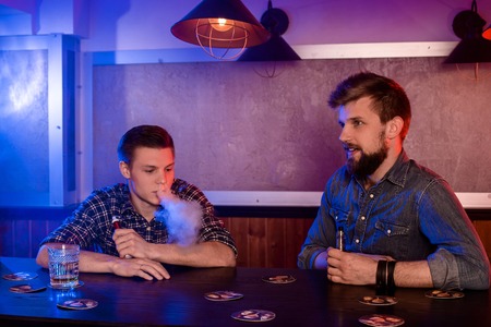 Vaping man holding a mod. A cloud of vapor at the vapebar.の写真素材