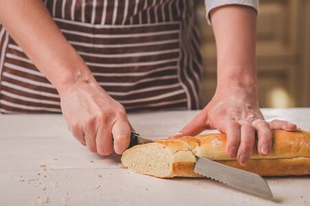 Woman cutting bread on wooden board. Bakehouse. Bread production. A woman in a striped apronの写真素材