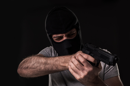 The robber in a mask with a gun pointed to the side on a black backgroundの写真素材
