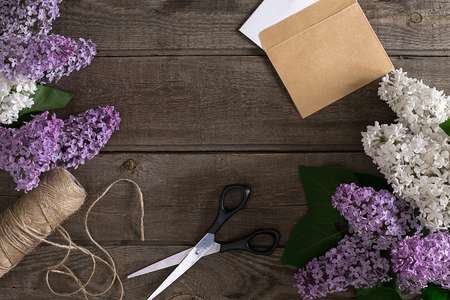 Lilac blossom on rustic wooden background with empty space for greeting message. Scissors, thread reel, small envelope. Top view. Mother's Day. Spring background concept.の写真素材