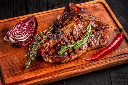 Medium rare grilled steak on rustic cutting board with rosemary and spices , dark rustic wooden background, top viewの写真素材